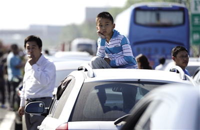 昨日,京沪高速天津段上,一名小男孩在车顶上遥望堵车长龙,甚至有车主在高速路上踢毽子、做体操消磨时间。廖攀 摄